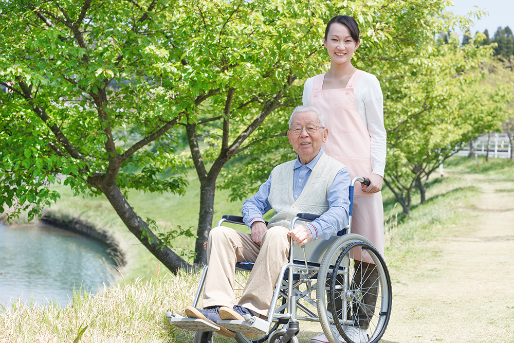 緑の自然の中で微笑む、車椅子の利用者様と介護士